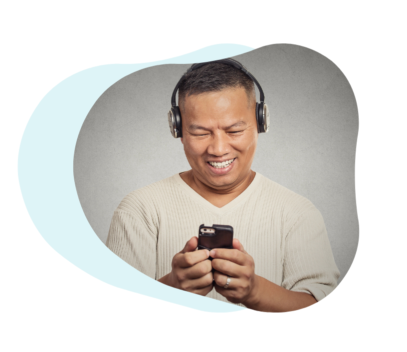 A smiling man wearing headphones, looking at his smartphone — engaging with a helpful video about his medication.