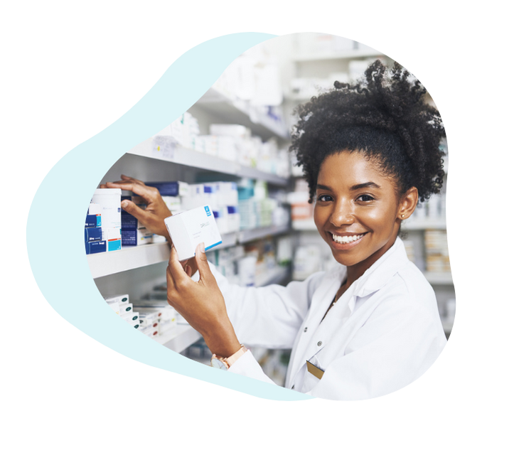 A smiling pharmacist standing in a pharmacy aisle, holding a box of medication — ready to help patients with safe and clear guidance.